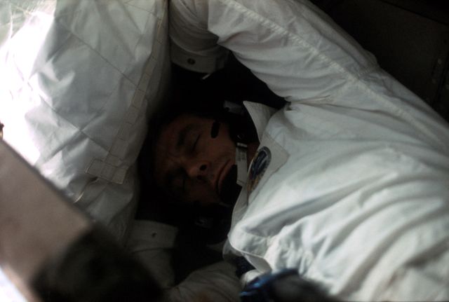 Astronaut Eugene Cernan rests aboard the Apollo 17 spacecraft during December 1972, the final mission of the NASA Apollo lunar landing program. This historic image captures a moment of rest during his important role as mission commander. Ideal for educational materials, documentaries on space exploration, historical archives, and illustrating human aspects of space missions.