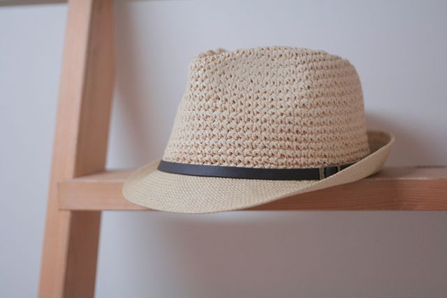 Brown woven fedora hat with black band placed on wooden shelf against neutral background. Ideal for fashion-related topics, wardrobe organization tips, or summer accessories.