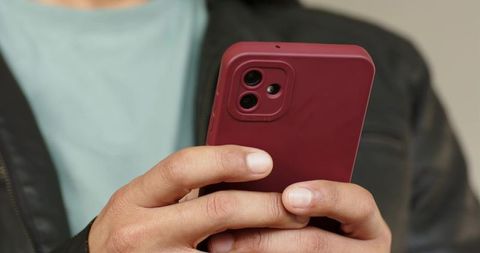 Closeup hands holding red smartphone scrolling and texting with dark jacket