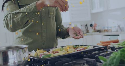 Home cook sprinkling herbs on roasting vegetables on stovetop for healthy dinner