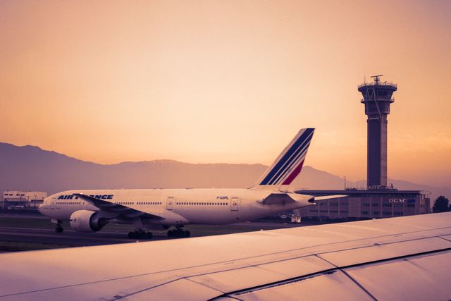 Air France airplane taxiing on a runway at sunset, with a control tower in the background. Ideal for travel blogs, aviation websites, and transport-related advertisements.