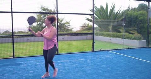 African american woman playing padel on blue court during outdoor fitness training session
