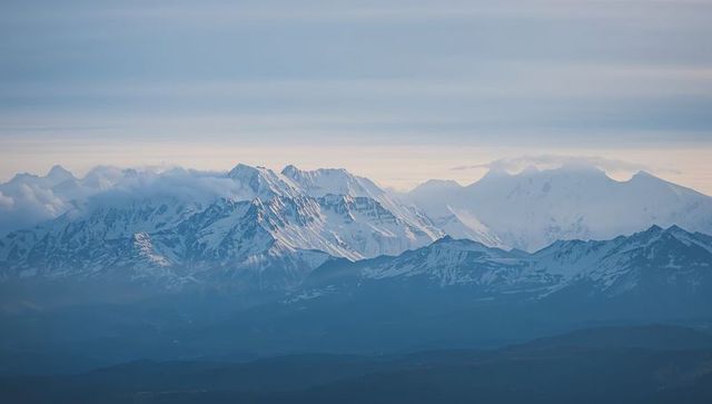 Blue Mist Rolling Over Snow-Capped Mountain Range at Sunrise, Remote Alpine Wilderness