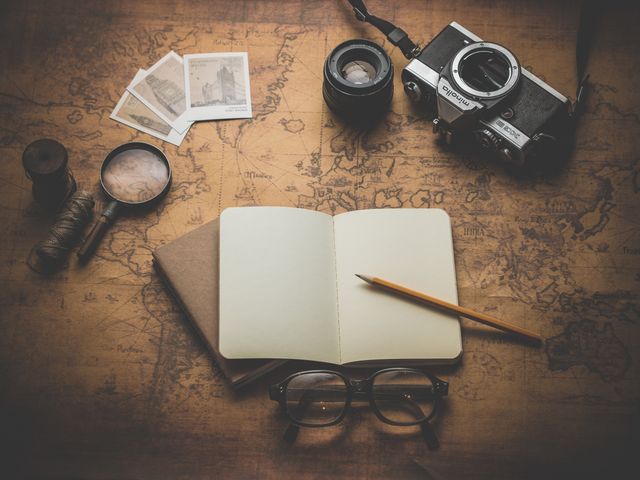 Vintage travel and exploration concept featuring an open journal, pencil, retro camera, and glasses on an antiquated map. Perfect for illustrating travel blog posts, adventure planning guides, and nostalgic themes.