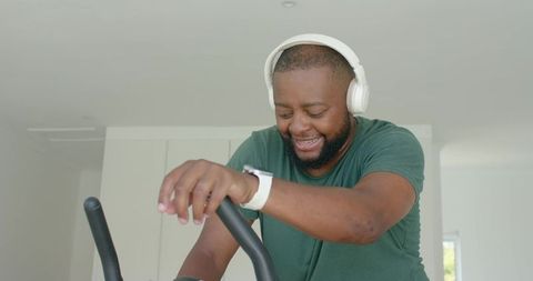 Smiling man pedaling on stationary bike at home, wearing headphones and smartwatch