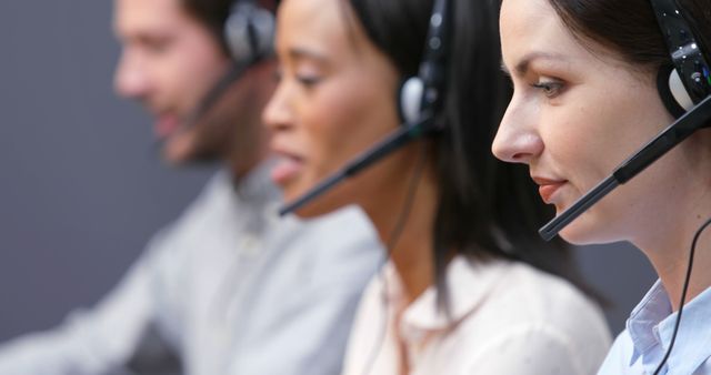 A diverse group of professionals, including Caucasian and Asian individuals, are working in a call center environment, with copy space. They are equipped with headsets, focused on providing customer support or managing inquiries.