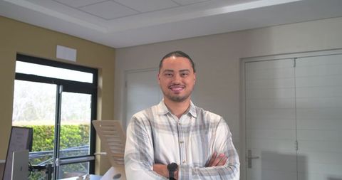Confident mid-adult man standing with arms crossed in modern reception workspace