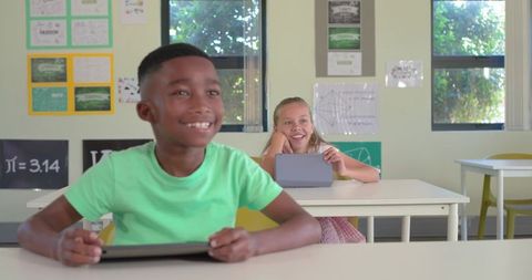 Smiling students using tablets in bright classroom, African American boy in green shirt