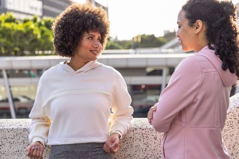 Sunlit african american friends chatting outdoors in hoodies and leggings on urban promenade