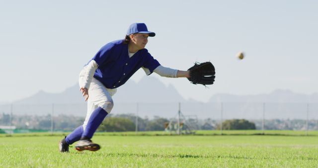 Teen boy wearing baseball uniform stretching to catch a ball during a game on a sunny day. Ideal for use in sports-related content, youth baseball promotions, and teamwork-themed marketing materials.