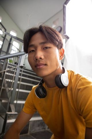 Asian teenager wearing headphones on urban staircase, casual youth portrait lifestyle