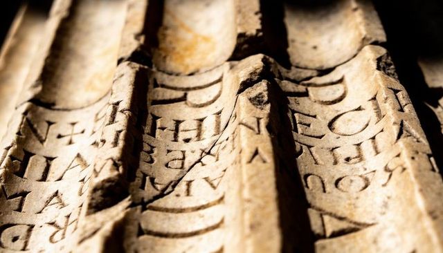 Weathered latin inscription showcasing fluted stone slab with diagonal crack and patina