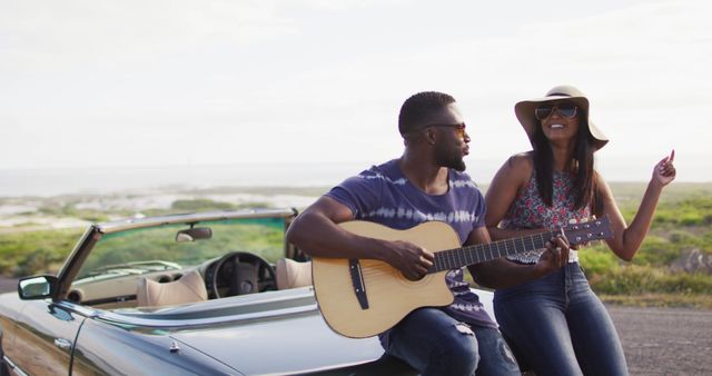 African american man playing guitar for his girlfriend while standing on the road. road trip travel and adventure concept
