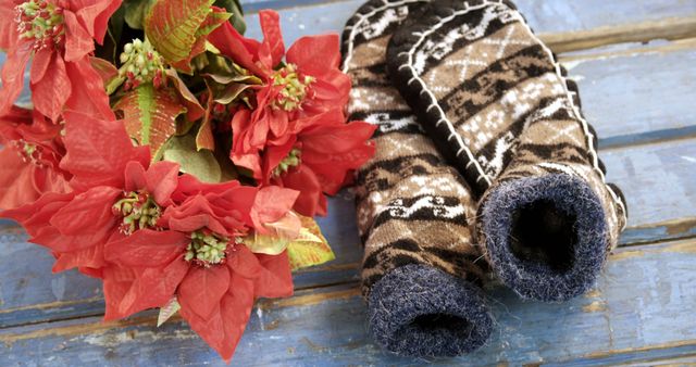 Close up of woollen christmas socks with shapes and red flowers on wooden table. Christmas and nature.