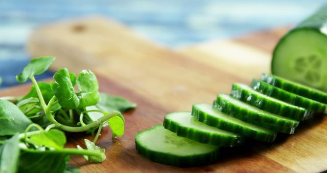 Fresh cucumber slices and green pea shoots are arranged on a wooden cutting board, with copy space. A healthy eating concept is depicted, emphasizing fresh produce and nutritious ingredients.