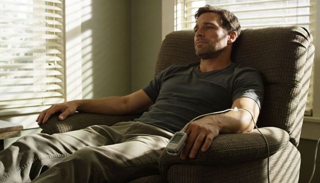 Reclining man receiving home iv infusion pump in sunlit living room, homecare and recovery