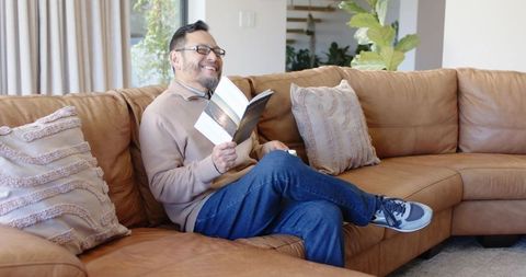 Senior man relaxing on leather sofa with book in modern living room