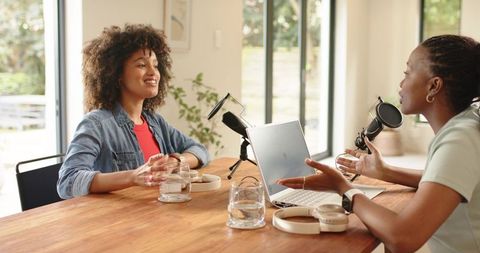 Recording podcast conversation between women in bright home studio with microphones