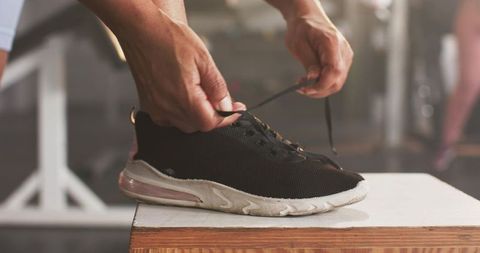 African american woman tying black sneaker on plyo box at gym during workout, close-up