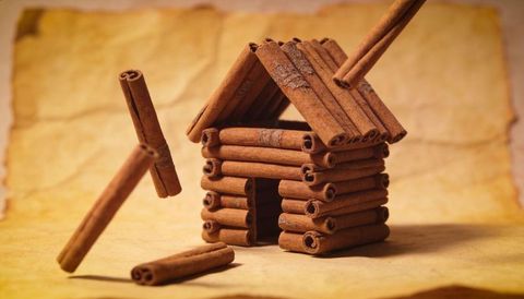 Miniature cinnamon stick log cabin on aged parchment tabletop warm rustic holiday craft