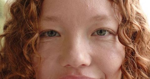 Closeup portrait redhead woman with freckles and curly hair, natural skin texture and soft light