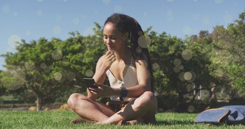 Woman with Smartphone Sitting on Grass Amid Glittering Spots