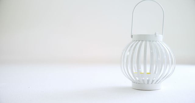 A white decorative lantern sits on a plain surface, with copy space. Its minimalist design suggests a modern home decor aesthetic.