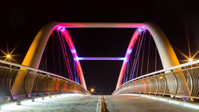 Modern bridge glowing with vibrant lights during night, showcasing architectural innovation and structural beauty. Ideal for use in urban design, architecture articles, transportation brochures, or cityscape photography collections.