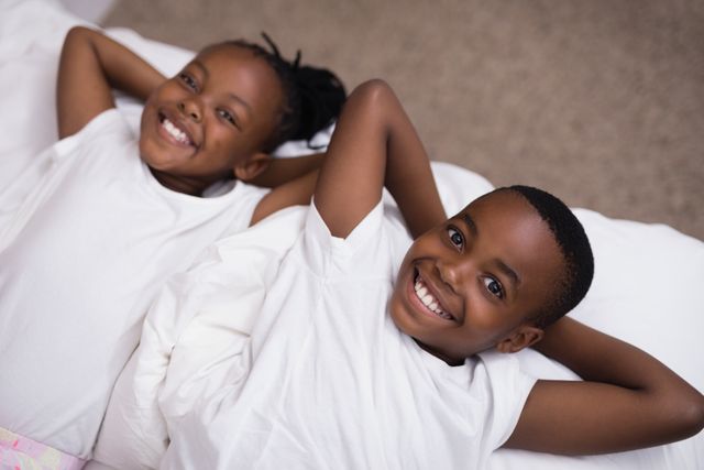 High angle portrait of smiling siblings lying together on bed at home