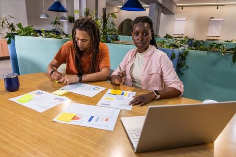 Multicultural coworkers collaborating over charts and laptop at communal coworking table