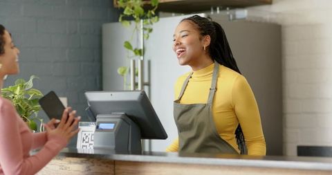Smiling black barista serving customer at rustic cafe counter with mobile payment