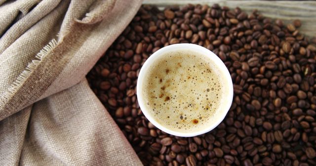 A freshly brewed cup of coffee sits amidst a scattering of whole coffee beans, with copy space. Its rich crema indicates a high-quality espresso shot, perfect for a caffeine boost or a coffee connoisseur's delight.