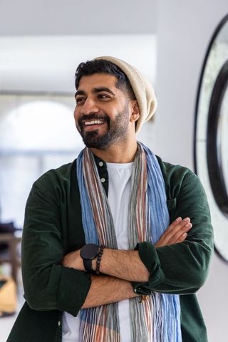 Bearded man smiling in bright living room wearing beanie and striped scarf
