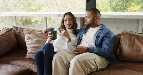 Couple relaxing on leather sofa sharing coffee and intimate conversation in sunlit room