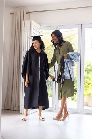 Graduate walking into home with proud mother holding jacket and purse