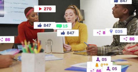 Team collaborating around laptop with social media engagement icons overlay for marketing