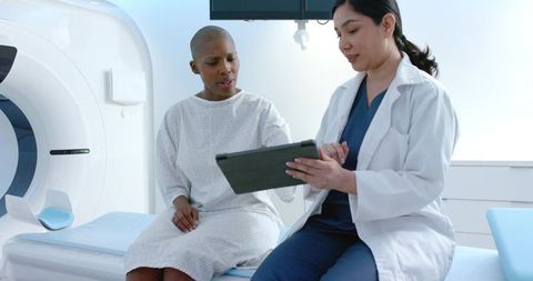 Diverse female patient and clinician reviewing ct scan on tablet in radiology suite