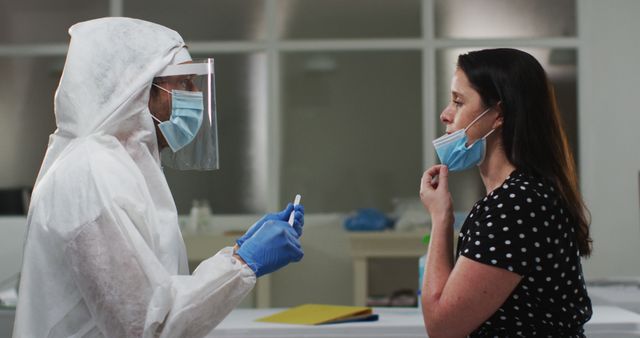 Healthcare worker in full PPE with mask, face shield, and gloves performing COVID-19 test on a woman adjusting her mask. Ideal for use in articles, health and safety materials, or informational content related to the pandemic, testing procedures, or healthcare services.
