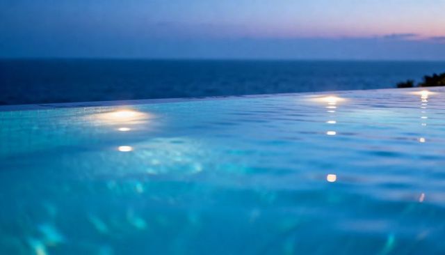 Infinity pool at dusk with glowing underwater lights reflecting on ocean horizon