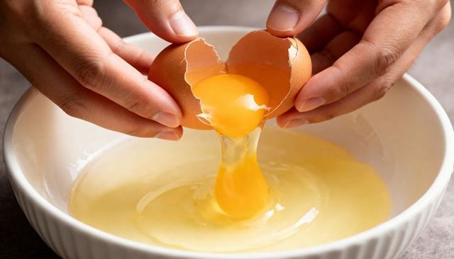Cracking brown egg revealing golden yolk pouring into white ceramic bowl for baking