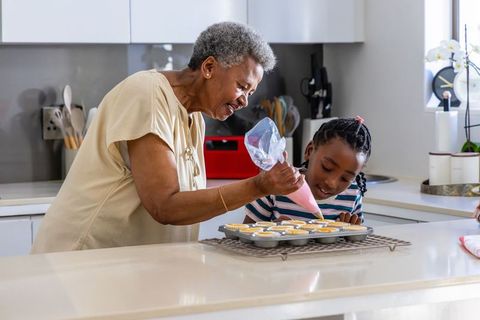 Senior african woman teaching granddaughter piping cupcakes in sunlit kitchen