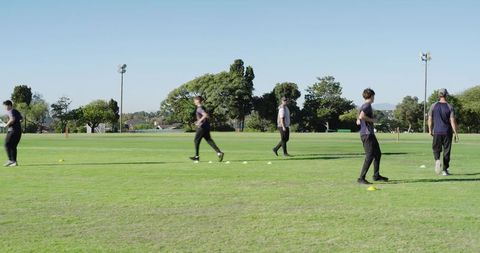 South asian coach guiding male trainees through cone drills on field for speed training