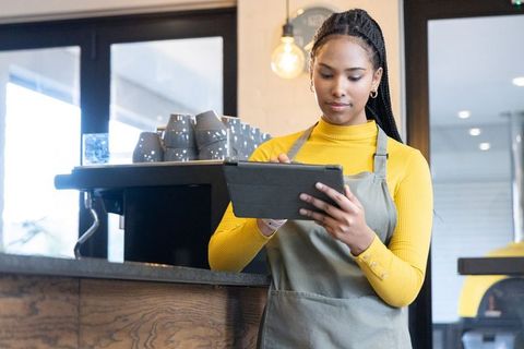 African american barista using tablet at modern cafe counter with espresso machine and gray cups