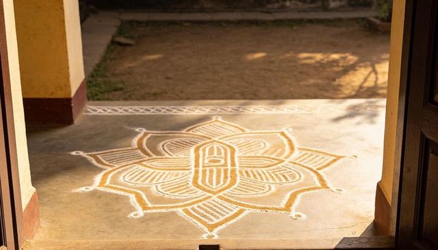 Sunlit floral rangoli at doorway with white outlines and golden yellow powder design