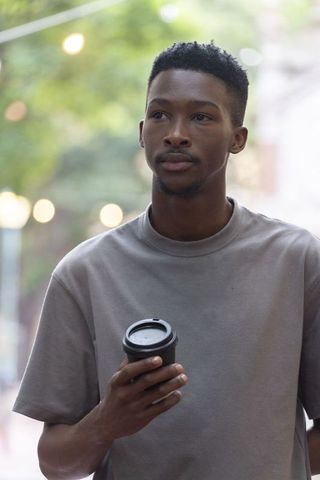 Thoughtful african man holding coffee cup on city street wearing grey tee urban lifestyle