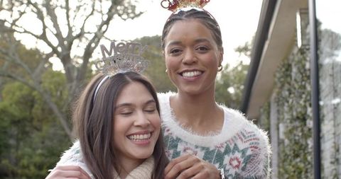 Two friends celebrating holiday season outdoors wearing festive headbands, cozy sweaters