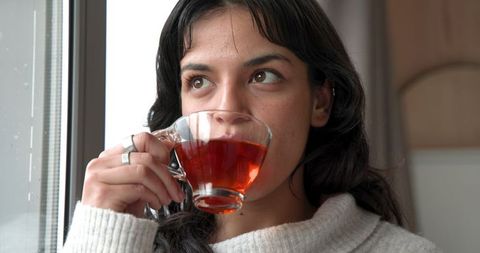 Young woman enjoying tea by window in cozy sweater