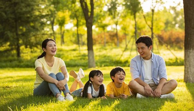 Family laughing, relaxing on park lawn at golden hour, parents with kids enjoying outdoors