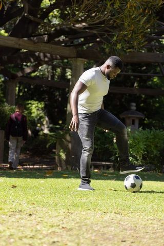 African man juggling soccer ball on sunlit park lawn under pergola