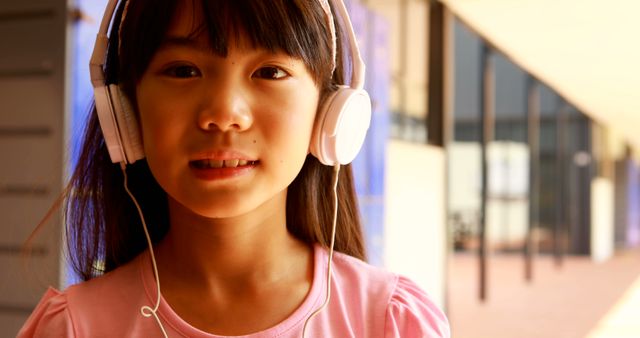 Young girl wearing headphones, listening to music outdoors. Perfect for use in educational material, advertising for children's headphones, music-related content, visualizations of happy childhood moments, and promoting children's leisure activities.